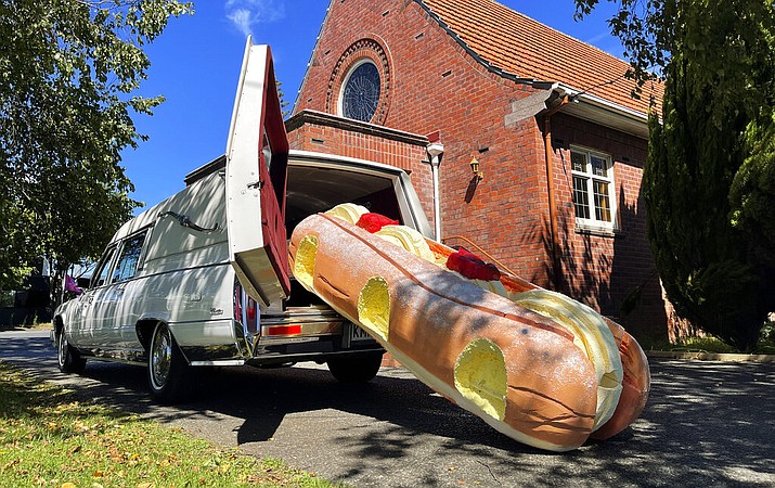 This photo provided by Ross Hall, shows a cream doughnut shaped coffin for the funeral of Phil McLean outside a church in Tauranga, New Zealand on Feb 17, 2021. Auckland company Dying Art makes unique custom caskets which reflect the people who will eventually lay inside them, whether it's a love for fire engines, a cream doughnut or Lego. (Ross Hall via AP)