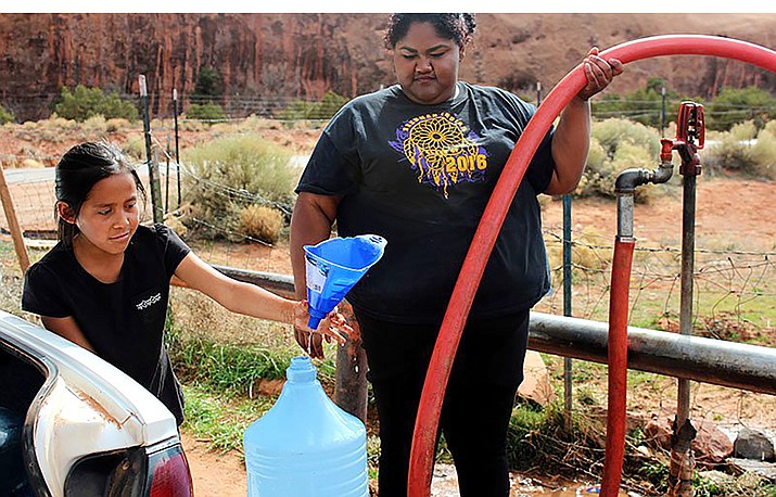 Zhane Atene, right, and her younger sister, Leighan, fill plastic containers with water to haul back home in this 2017 file photo. Lack of running water is just one of the many infrastructure problems on tribal lands, officials told a House panel Wednesday. (File photo by Devon Cordell/Cronkite News)