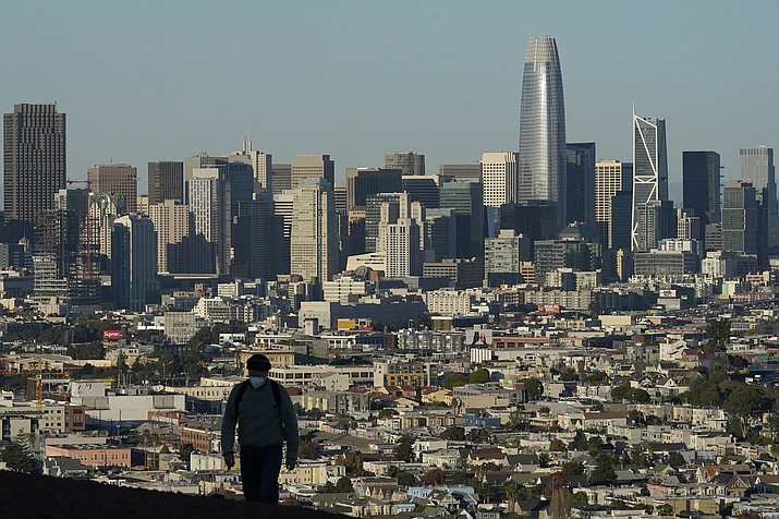 In this Dec. 7, 2020 photo, a person wearing a protective mask walks in front of the skyline on Bernal Heights Hill during the coronavirus pandemic in San Francisco. California's population has declined for the first time in its history. State officials announced Friday, May 7, 2021, that the nation's most populous state lost 182,083 people in 2020. California's population is now just under 39.5 million. (Jeff Chiu/AP, File)