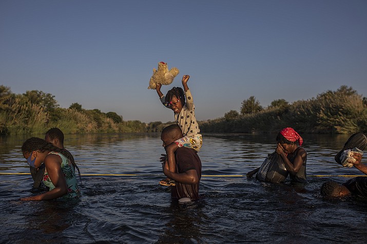 A little girl holds her stuffed animal high above the water as migrants, many from Haiti, wade across the Rio Grande river from Del Rio, Texas, to return to Ciudad Acuña, Mexico, Monday, Sept. 20, 2021, to avoid deportation. The U.S. is flying Haitians camped in a Texas border town back to their homeland and blocking others from crossing the border from Mexico. (Felix Marquez/AP)