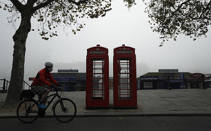 A cyclist wearing a face mask passes traditional red phone boxes, in London, on Nov. 5, 2020. Thousands of Britain’s iconic red phone boxes will be protected from removal under new rules, the telecoms regulator said Tuesday, Nov. 9, 2021. (Matt Dunham/AP, File)
