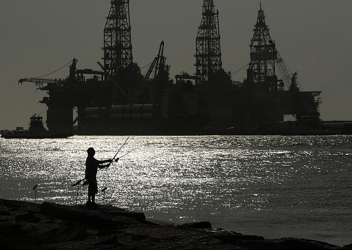 A man wears a face mark as he fishes near docked oil drilling platforms, Friday, May 8, 2020, in Port Aransas, Texas. The U.S. Interior Department on Wednesday, Nov. 17, 2021, is auctioning vast oil reserves in the Gulf of Mexico estimated to hold up to 1.1 billion barrels of crude. It's the first such sale under President Joe Biden and underscores the challenges he faces to reach climate goals that rely on cuts in fossil fuel emissions. (Eric Gay/AP, File)