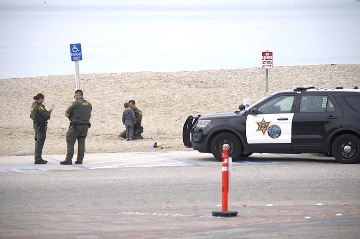 A missing 3-year-old boy from Tennessee stands on the beach with Orange County Sheriff's deputies at Doheny State Beach in Dana Point, Calif., Thursday, Nov. 18, 2021. The missing boy from Tennessee and a 16-year-old girl from Kentucky were found safe in Southern California and the younger child's father was arrested, authorities said. Deputies found Noah Clare and his cousin, Amber Clare, Thursday morning the Orange County Sheriff's Department said. (Patrick Smith via AP)