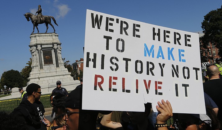 In this Saturday, Sept. 16, 2017 photo, protesters hold signs in front of the statue of Confederate General Robert E. Lee on Monument Avenue in Richmond, Va. A jury began deliberations Friday, Nov. 19, 2021 in a civil trial of white nationalists accused of conspiring to commit racially motivated violence at the deadly “Unite the Right" rally in Charlottesville four years ago.(Steve Helber/AP, File)