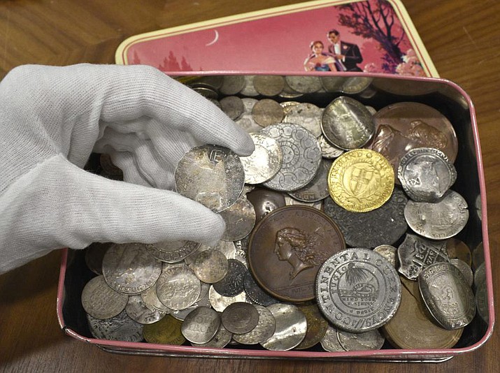 In this Sept. 9, 2021 photo, a rare 17th century one shilling coin is displayed above a metal box containing other coins, at the auction house, in London. Morton & Eden Ltd. says the extraordinarily rare coin, with a face value of just pennies when it was minted in mid-17th century New England, sold for the equivalent of $350,000. (Menelaos Danellis/Morton & Eden Ltd. via AP)