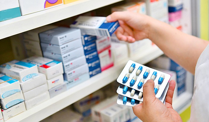Pharmacist holding medicine box and capsule pack in pharmacy drugstore. (viewfinder/Shutterstock)