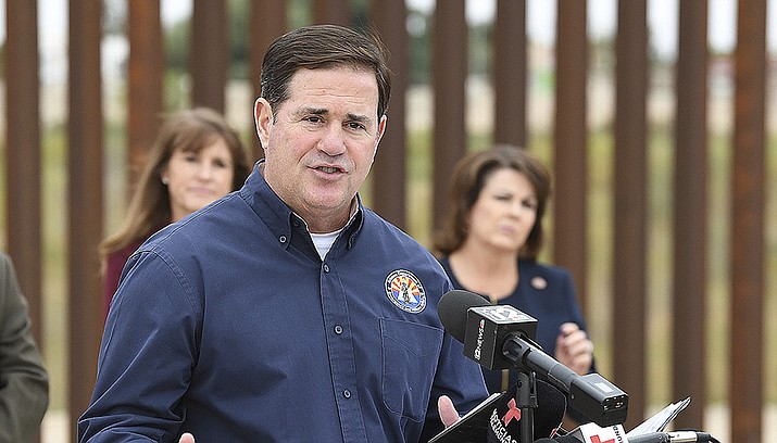 Arizona Gov. Doug Ducey addresses the media Tuesday afternoon, Dec. 7, 2021, on the Yuma Levee Road near County 8 1/2 Street in the Yuma Valley, near Yuma, Ariz., along the Colorado River, Morelos Dam and the United States-Mexico border. Yuma Mayor Doug Nicholls says an emergency situation in the southwestern Arizona border city has eased with federal officials moving in additional personnel in response to thousands of migrants.(Randy Hoeft/The Yuma Sun via AP)