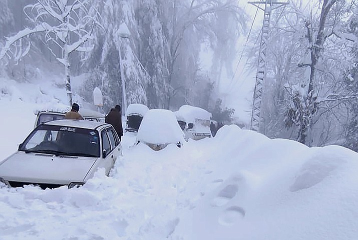 In this photo provided by the Inter Services Public Relations, people walk past vehicles trapped in a heavy snowfall-hit area in Murree, some 28 miles (45 kilometers) north of the capital of Islamabad, Pakistan, Saturday, Jan. 8, 2022. Temperatures fell to minus 8 degrees Celsius (17.6 Fahrenheit) amid heavy snowfall at Pakistan's mountain resort town of Murree overnight, killing multiple people who were stuck in their vehicles, officials said Saturday. (Inter Services Public Relations via AP)