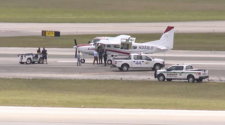 This still image from video shows emergency personnel surrounding a Cessna plane at Palm Beach International Airport Tuesday, May 10, 2022, in West Palm Beach, Fla. A passenger with no flying experience was able to land the plane safely with help of air traffic controllers after the pilot was too sick to handle the controls. (WPTV via AP)
