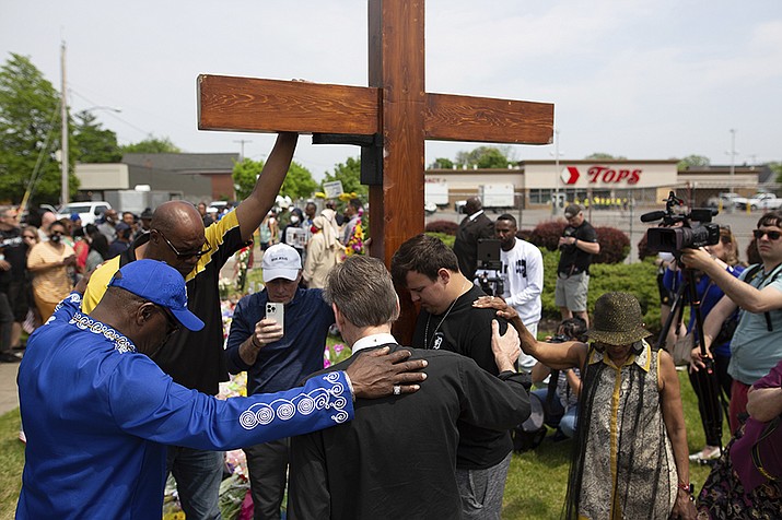 A group prays at the site of a memorial for the victims of the Buffalo supermarket shooting outside the Tops Friendly Market on Saturday, May 21, 2022, in Buffalo, N.Y. Tops was encouraging people to join its stores in a moment of silence to honor the shooting victims Saturday at 2:30 p.m., the approximate time of the attack a week earlier. Buffalo Mayor Byron Brown also called for 123 seconds of silence from 2:28 p.m. to 2:31 p.m., followed by the ringing of church bells 13 times throughout the city to honor the 10 people killed and three wounded. (Joshua Bessex/AP)