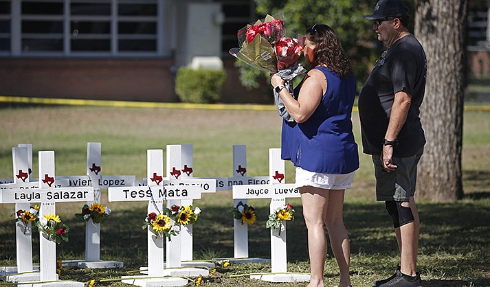 A couple prepare to place flowers on crosses with the names of children killed outside of the Robb Elementary School in Uvalde, Texas Thursday, May 26, 2022. (AP Photo/Dario Lopez-Mills)