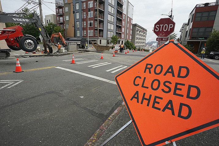 A sign is shown near ongoing work on a project to replace water main pipes, Wednesday, June 15, 2022, in downtown Tacoma, Wash. Inflation is taking a toll on infrastructure projects across the U.S., driving up costs so much that state and local officials are postponing projects, scaling back others and reprioritizing their needs. (Ted S. Warren/AP)