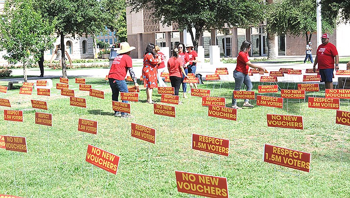 Members of Save Our Schools Arizona erect signs on the lawn at the Capitol Wednesday urging lawmakers to reject universal vouchers and honor the will of voters who four years ago voting against expansion. (Photo by Howard Fischer/For the Miner)