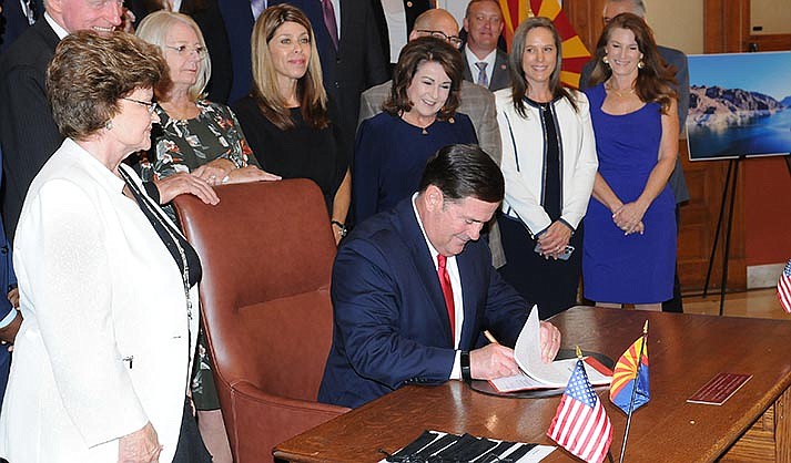 Surrounded by state lawmakers, Gov. Doug Ducey on Wednesday signs legislation that will put $1.2 billion into projects to acquire new sources of water and conserve what the state already has. (Capitol Media Services photo by Howard Fischer)