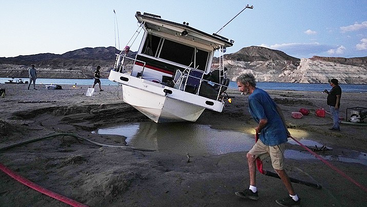 Craig Miller hauls a hose while trying to free his stranded houseboat at the Lake Mead National Recreation Area, Thursday, June 23, 2022, near Boulder City, Nev. Miller had been living on the stranded boat for over two weeks after engine trouble and falling lake levels left the boat above the water level. (AP Photo/John Locher)
