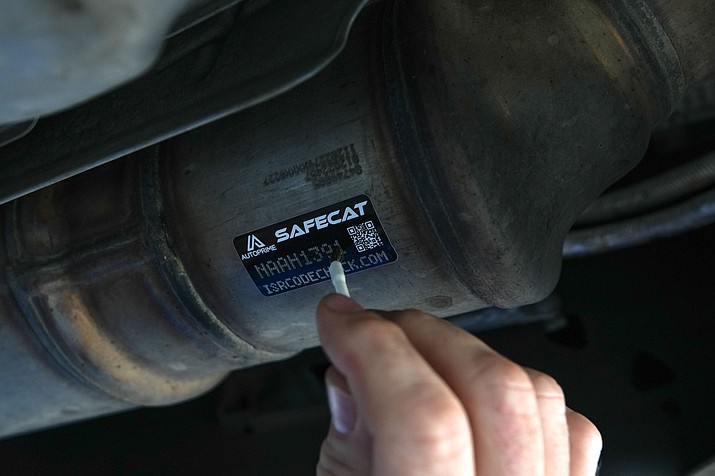 A mechanic at Courtesy Chevrolet in Phoenix applies acid to a Safecat sticker on July 20, 2022. The acid will eat into the metal through the perforations in the sticker, etching the code onto the catalytic converter. (Troy Hill/Cronkite News)
