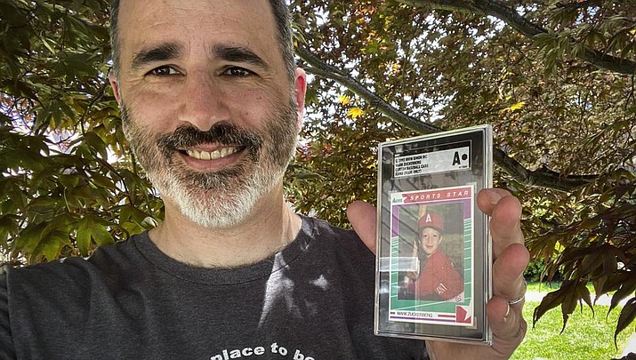 Allie Tarantino holds a baseball card featuring a very young Mark Zuckerberg grinning in a red jersey and gripping a bat. For 30 years Tarantino kept the baseball card filed away in his basement, not knowing Zuckerberg would someday become a household name. (Shira Tarantino via AP)