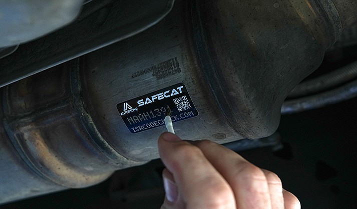 A mechanic at Courtesy Chevrolet in Phoenix applies acid to a Safecat sticker on July 20, 2022. The acid will eat into the metal through the perforations in the sticker, etching the code onto the catalytic converter. (Photo by Troy Hill/Cronkite News)