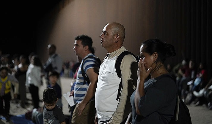 Migrants from Colombia, front, wait to be processed by Border Patrol agents near the end of a border wall Tuesday, Aug. 23, 2022, near Yuma, Arizona. The Border Patrol is seeing a dramatic shift in the type of migrants who come across the busiest places on the U.S.-Mexico. Migrants are now coming from more than 100 countries, and Mexicans are virtually absent. (AP Photo/Gregory Bull)