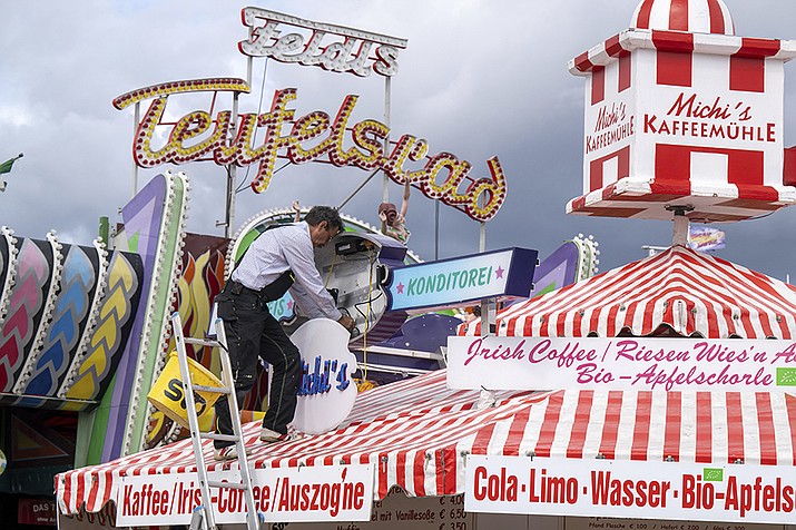 A man mounts a light advertisement on a booth on the Oktoberfest grounds in Munich, Germany, Thursday, Sept. 15, 2022. The Oktoberfest is on tap again in Germany after a two-year pandemic interruption. The beer will be just as cold and the pork knuckle just as juicy. But brewers and visitors are under pressure from inflation in ways they could hardly imagine in 2019. (Peter Kneffel/dpa via AP)