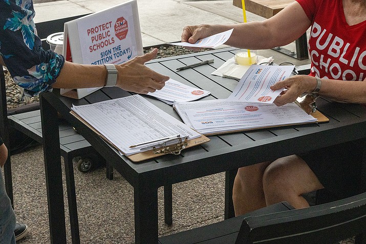 A volunteer collects signatures in Phoenix on Wednesday for the Save Our Schools Arizona petition that would stall the expansion of the state’s empowerment scholarship accounts — school vouchers — and put the issue on the 2024 ballot. (Justin Spangenthal/Cronkite News)