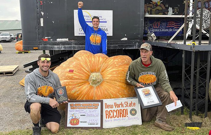 In this photo, Emmett Andrusz, from left, Steve Andrusz and Scott Andrusz, pose with the record setting 2,554-pound pumpkin, in Clarence, N.Y., Saturday, Oct. 1, 2022. Scott Andrusz's entry broke the previous record of 2,528 pounds. (The Great Pumpkin Farm via AP)