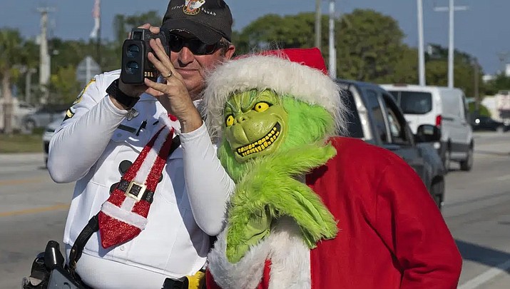 Monroe County Sheriff's Office Col. Lou Caputo, right, costumed as the Grinch, leans on the shoulder of Deputy Andrew Leird, left, as he uses a laser speed detector to check speeds of motorists traveling through a school zone on the Florida Keys Overseas Highway Tuesday, Dec. 13, 2022, in Marathon, Fla. For drivers slightly speeding through the area, Caputo offers them the choice between an onion or a traffic citation. (Andy Newman/Florida Keys News Bureau via AP)