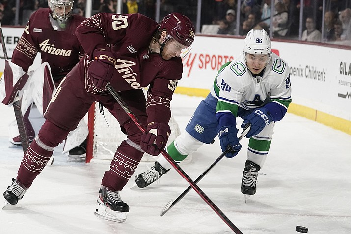 Vancouver Canucks' Andrei Kuzmenko (96) chases the puck against Arizona Coyotes' J.J. Moser (90) during the first period of a game Thursday, March 16, 2023, in Tempe, Ariz. (Darryl Webb/AP)
