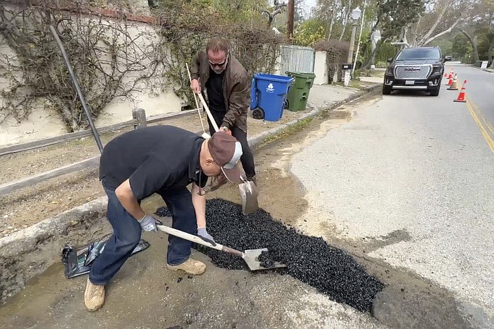 This video still image provided by The Office of Arnold Schwarzenegger, shows former California Governor Arnold Schwarzenegger, center back, repairing a pot hole on a street in his Los Angeles neighborhood on Tuesday, April 11, 2023. (The Office of Arnold Schwarzenegger via AP)