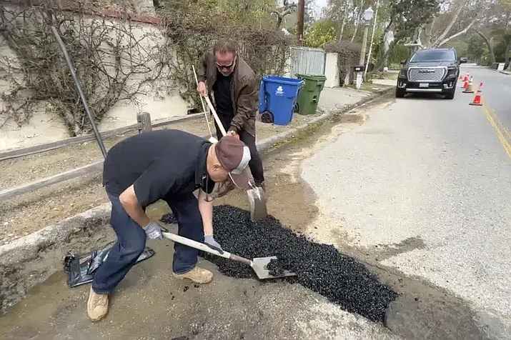 This video still image provided by The Office of Arnold Schwarzenegger, shows former California Governor Arnold Schwarzenegger, center back, repairing a pot hole on a street in his Los Angeles neighborhood on Tuesday, April 11, 2023. Fed up by an enormous pothole in his neighborhood, Schwarzenegger picked up a shovel and filled it himself. (The Office of Arnold Schwarzenegger via AP)