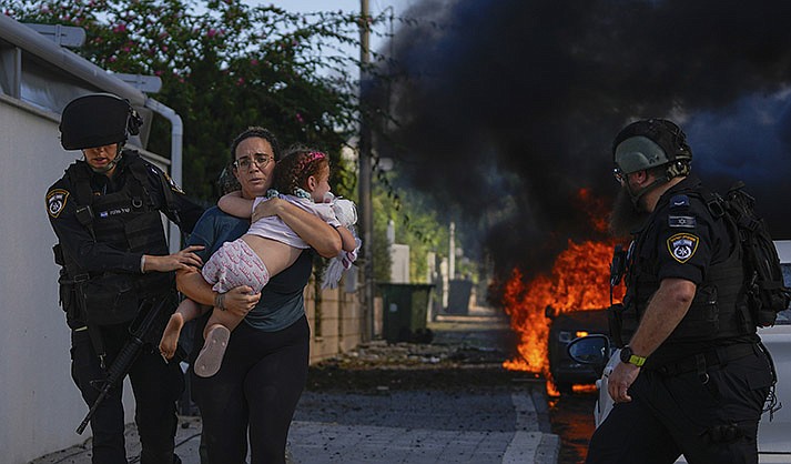 Police officers evacuate a woman and a child from a site hit by a rocket fired from the Gaza Strip, in Ashkelon, southern Israel, Saturday, Oct. 7, 2023. The rockets were fired as Hamas announced a new operation against Israel. (AP Photo/Tsafrir Abayov, File)
