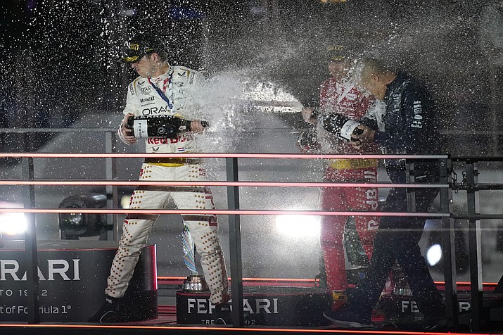 Red Bull driver Max Verstappen, of the Netherlands, left, Sergio Perez, of Mexico, center, and an unidentified person at right, celebrate after a first and second place finish, Sunday, Nov. 19, 2023, in Las Vegas. (John Locher/AP)