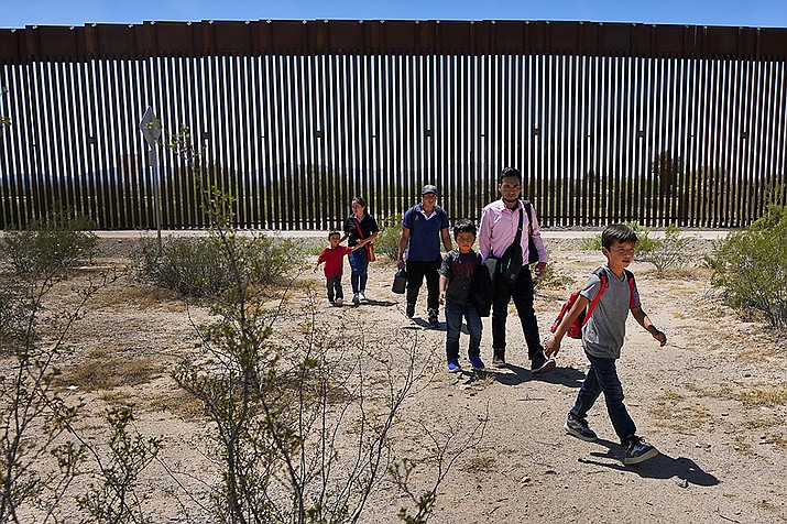 A family of five claiming to be from Guatemala and a man stating he was from Peru, in pink shirt, walk through the desert after crossing the border wall in the Tucson Sector of the U.S.-Mexico border, Aug. 29, 2023, in Organ Pipe Cactus National Monument near Lukeville, Ariz.  Customs and Border Protection is closing down the port of entry in Lukeville, a remote desert crossing that has become a major migration route in recent months. (Matt York, AP File)