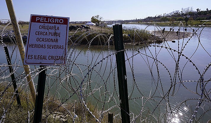 Migrants cross the Rio Grande into the U.S. from Mexico behind Concertina wire and a sign warning that it's dangerous and illegal to cross, Wednesday, Jan. 3, 2024, in Eagle Pass, Texas. According to U.S. officials, a Mexican enforcement surge has contributed to a sharp drop in illegal entries to the U.S. in recent weeks. (AP Photo/Eric Gay)